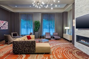 A modern hotel lobby with a sofa, chairs, a fireplace, and large windows. - Residence Inn by Marriott Charlottesville Downtown (Charlottesville)