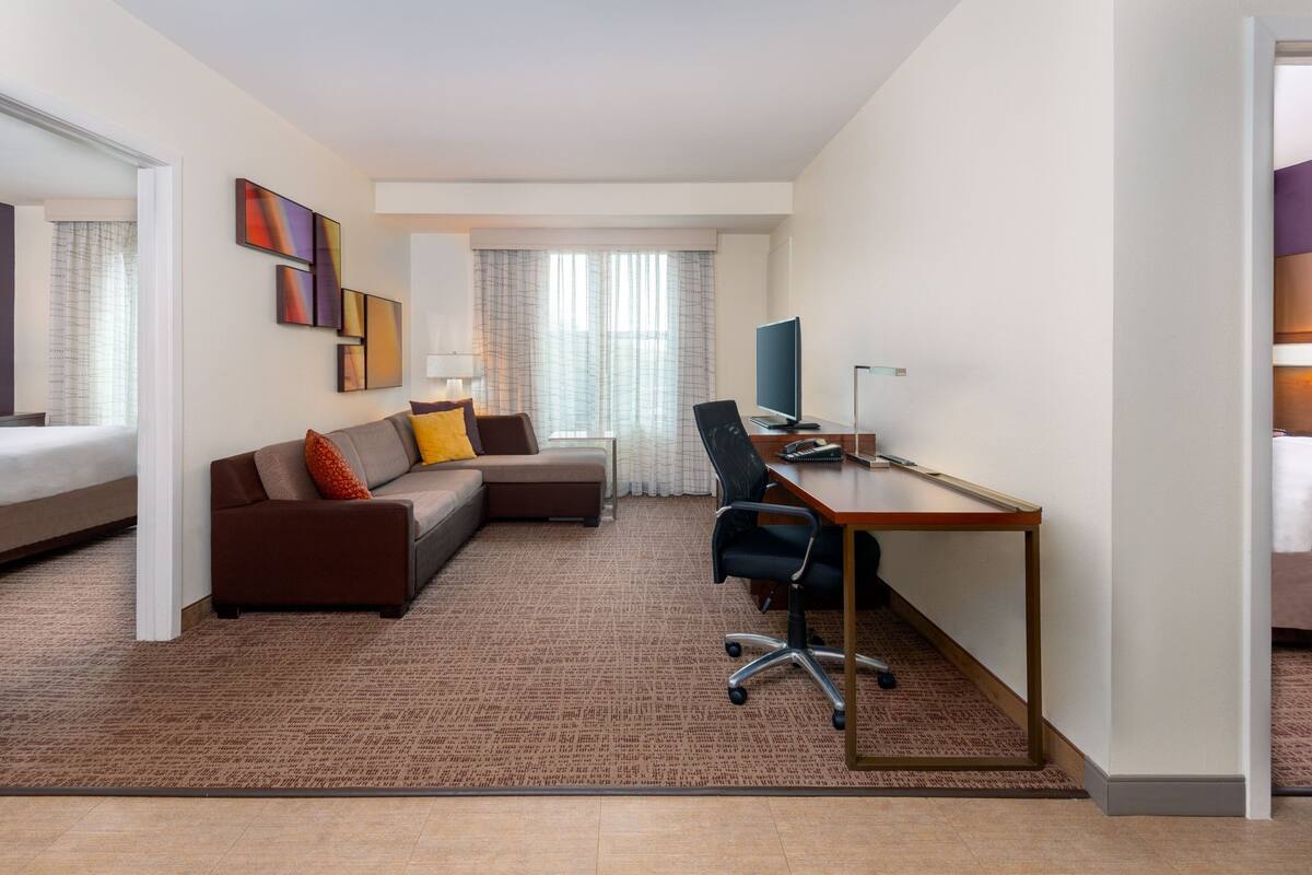 A modern hotel room with a sofa, a desk, and a television.