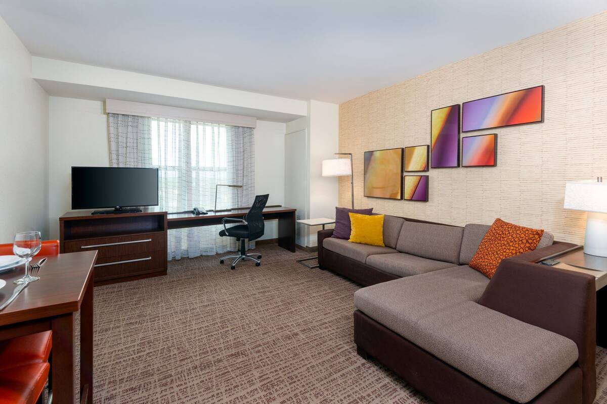 A hotel room with a sofa, a desk, a television, and artwork on the wall.