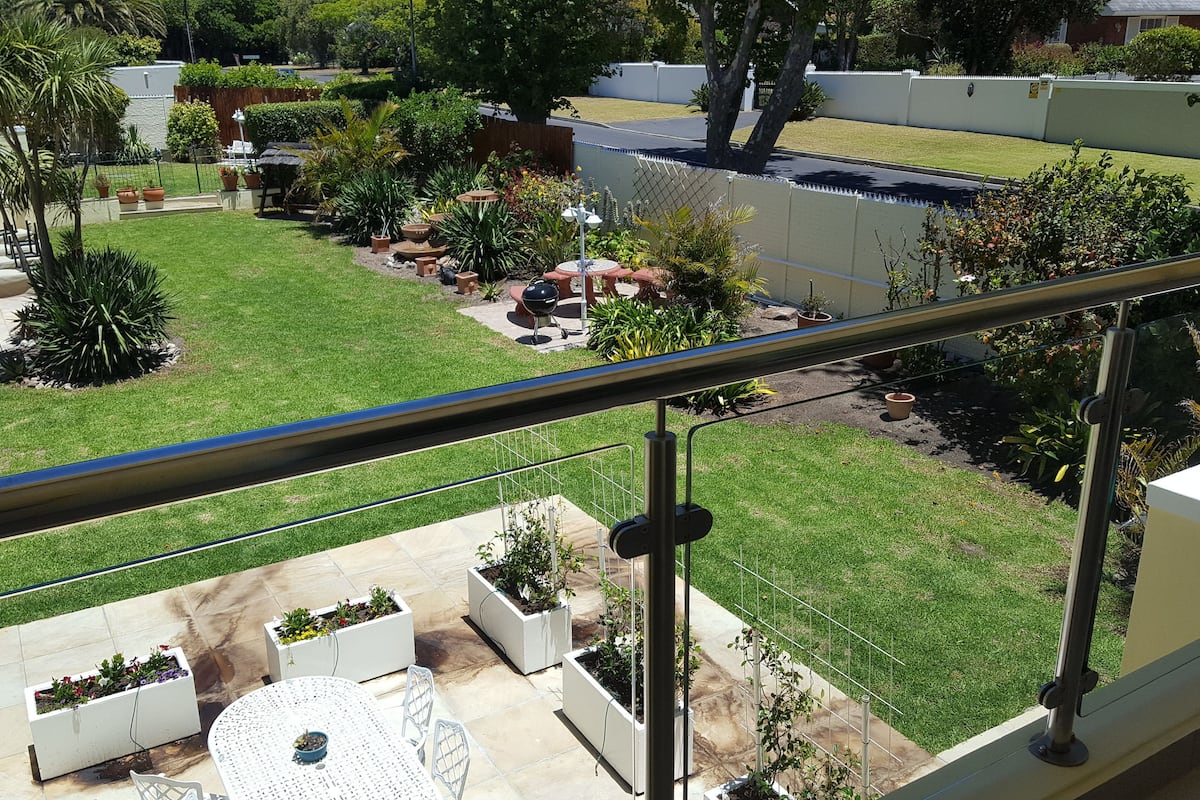 A residential backyard with a swimming pool, a patio area with outdoor furniture, and a variety of potted plants and trees.