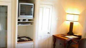 A room with a built-in TV shelf, a desk with a lamp, and a door. - The Royal Hotel (Riebeek Kasteel)
