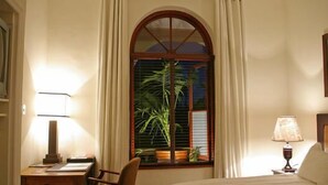 A hotel room with a bed, a desk with a lamp, a chair, a window with curtains, and a wall-mounted clock. - The Royal Hotel (Riebeek Kasteel)