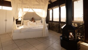 A bedroom with a canopy bed, a stone wall, and a fireplace. - Vingerklip Lodge (Khorixas)
