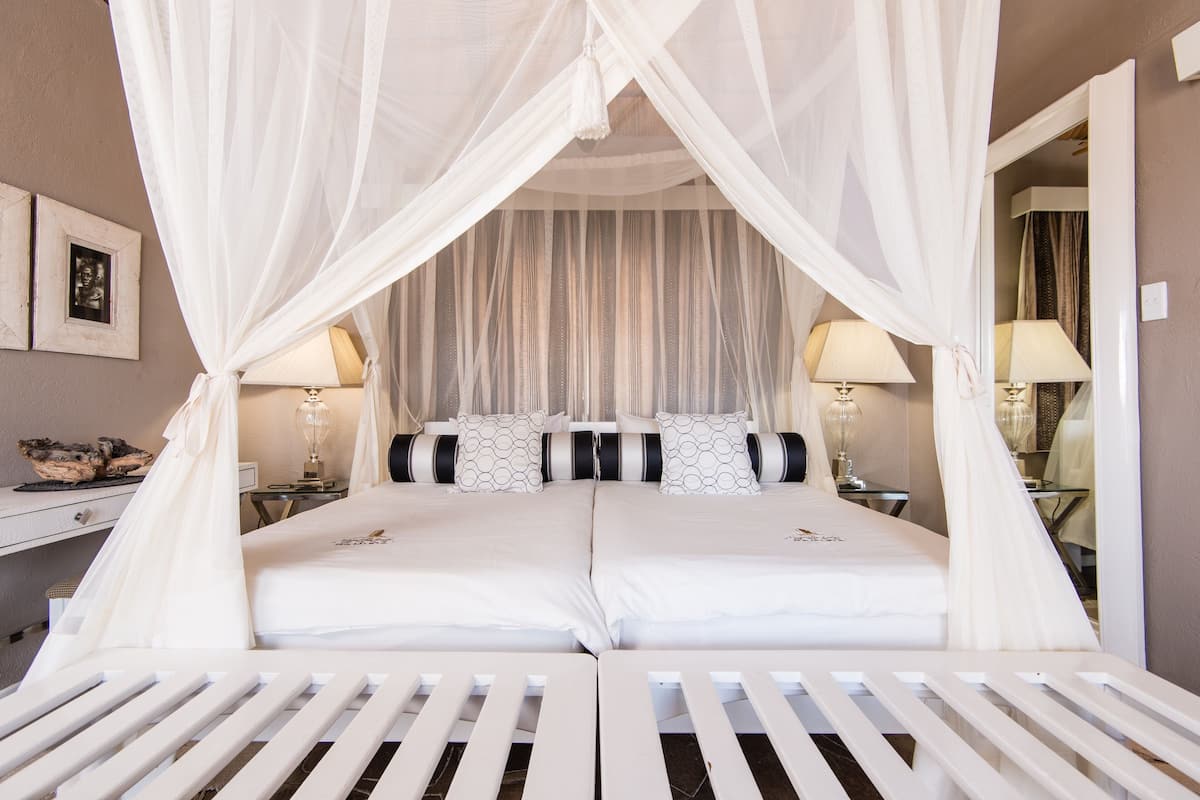 A double bed with white bedding and a canopy, two bedside tables with lamps, a mirror, and a picture frame on the wall.