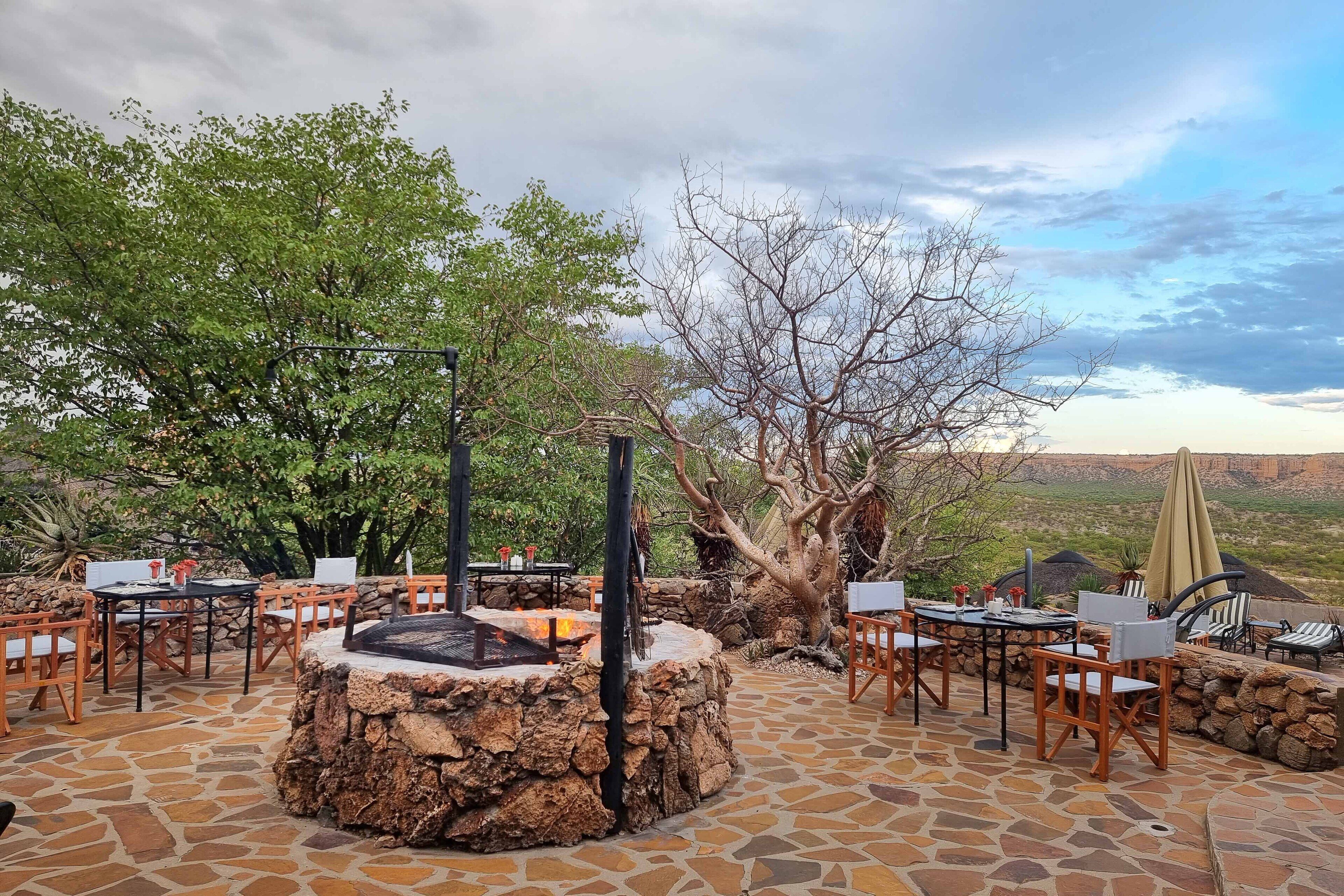 Une terrasse extérieure avec un sol en pierre, des tables, des chaises et un foyer central.