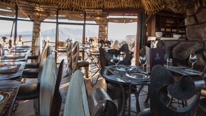 An outdoor dining area with thatched roof, tables set for dining, and a view of the landscape. - Vingerklip Lodge (Khorixas)