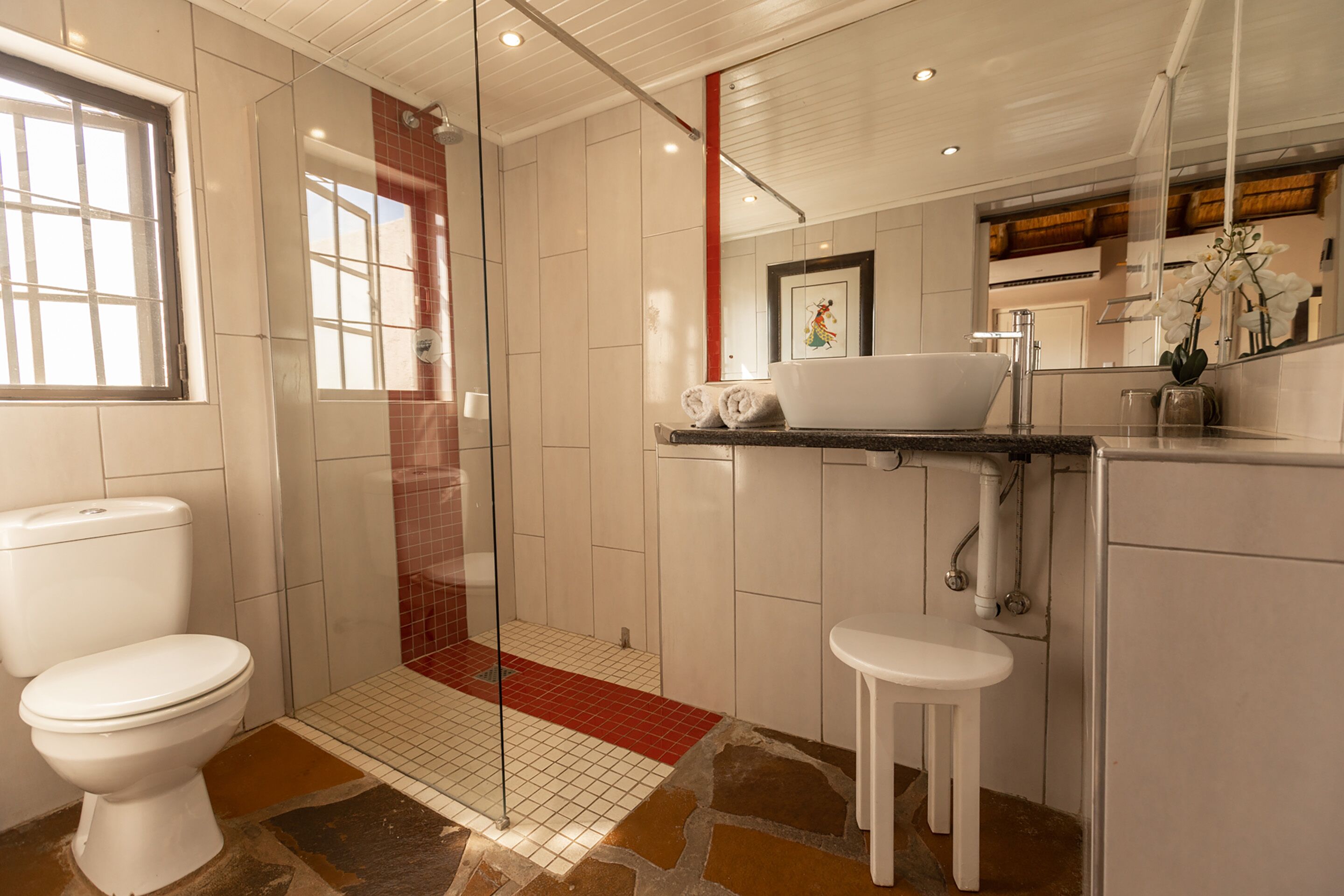 A modern bathroom with a toilet, shower, sink, and a small stool.