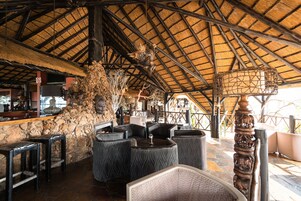 An indoor seating area with stone walls, a thatched roof, and a bar counter.