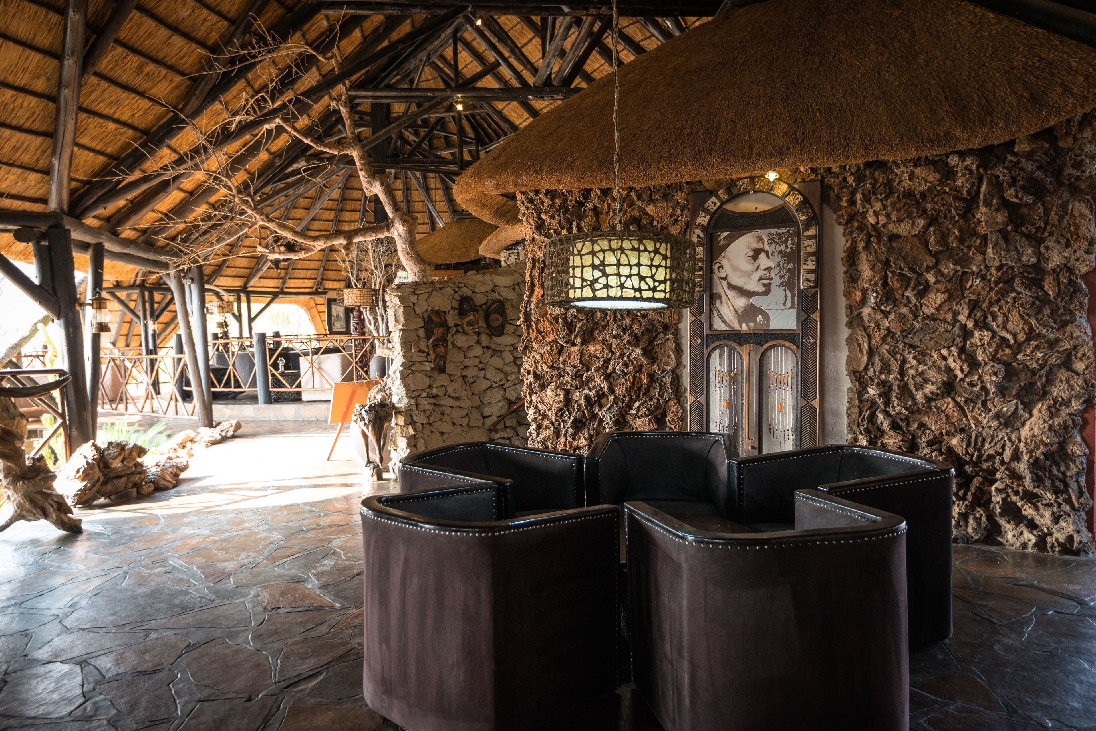 A rustic interior with stone walls, a thatched roof, and leather seating.