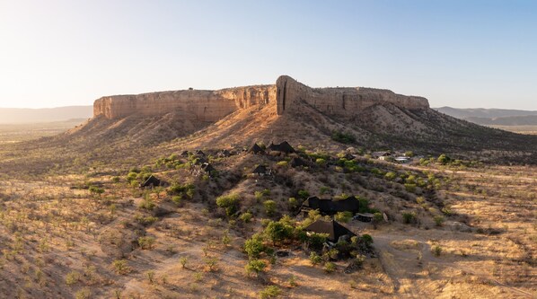 A large, flat-topped mesa with sparse vegetation and a few small buildings at its base. - Vingerklip Lodge (Khorixas)