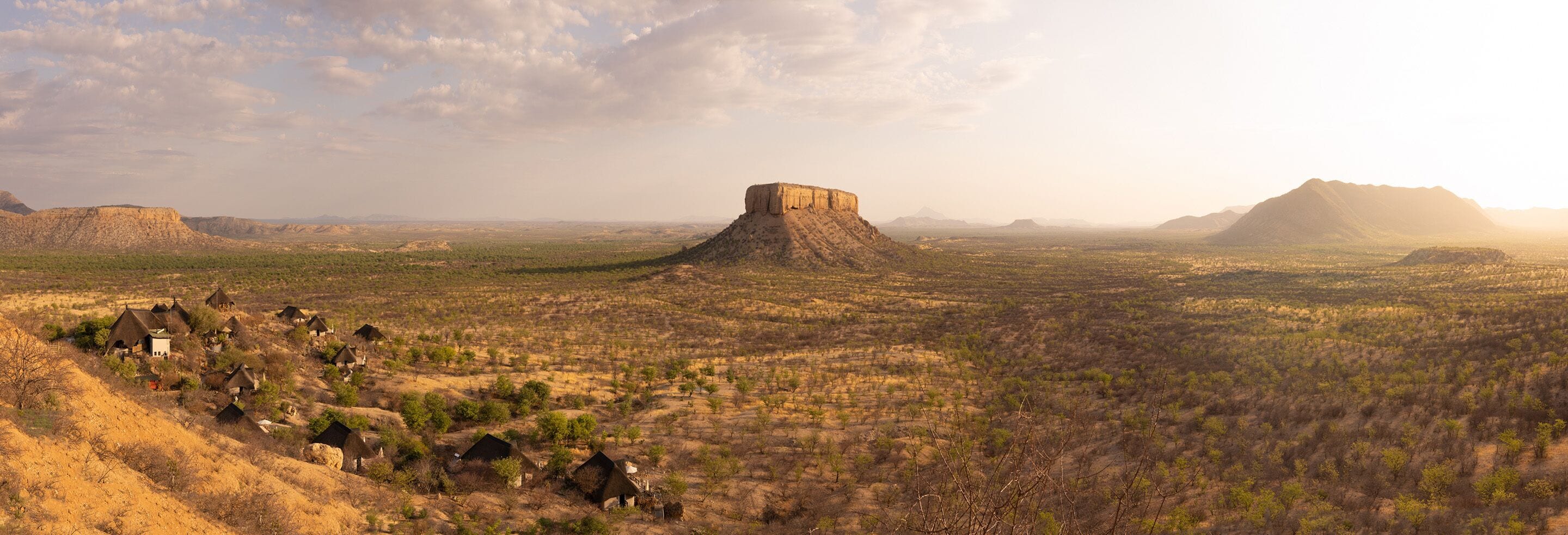 A landscape with a prominent hill and a small settlement with traditional huts.