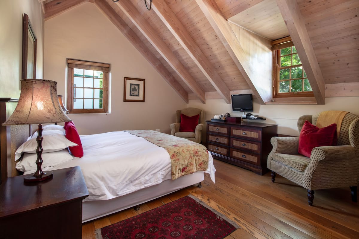 A bedroom with a sloped ceiling, a bed, a dresser, a chair, and a television.