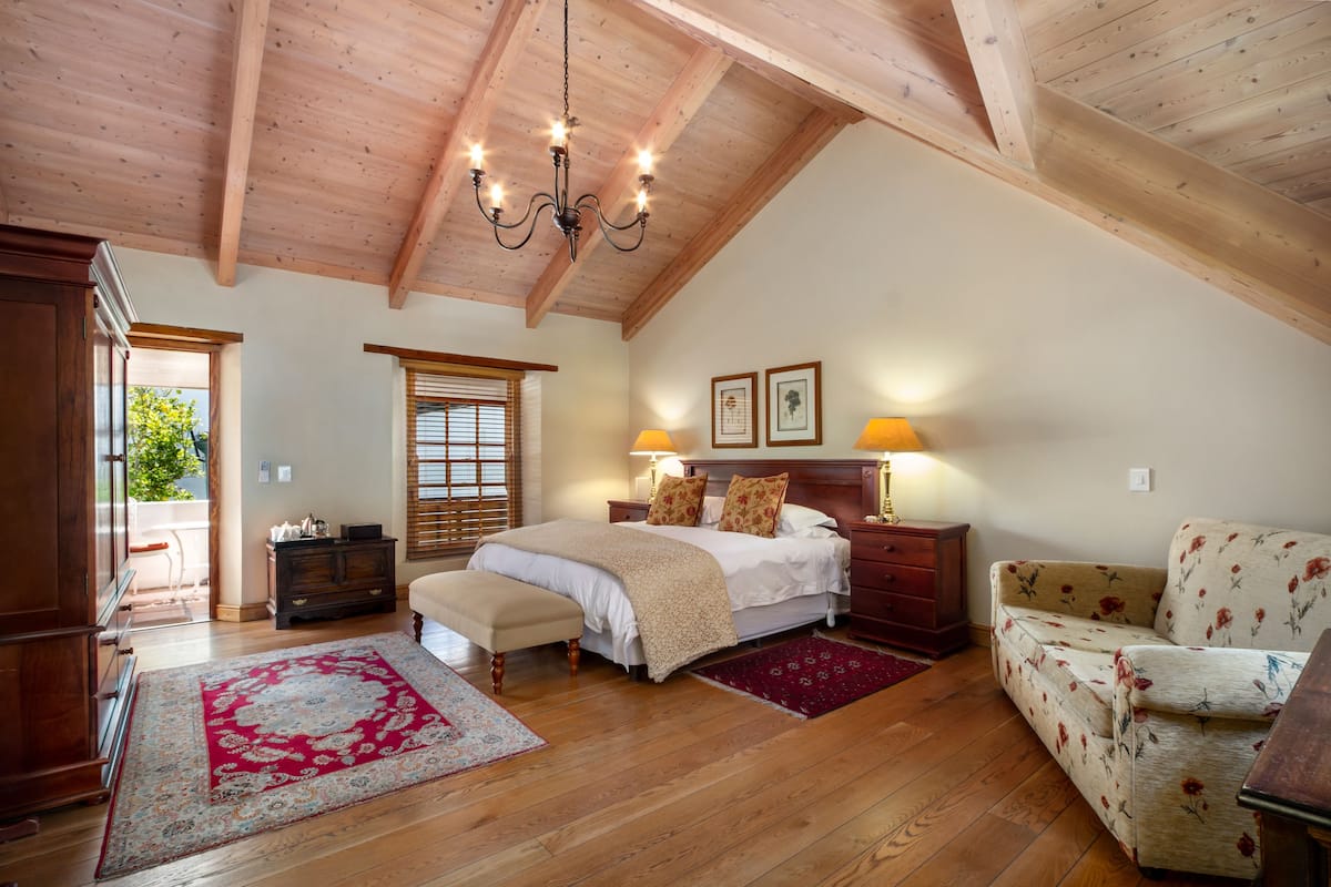 A bedroom with a wooden ceiling, a large bed, a bench, a sofa, and a nightstand with lamps.