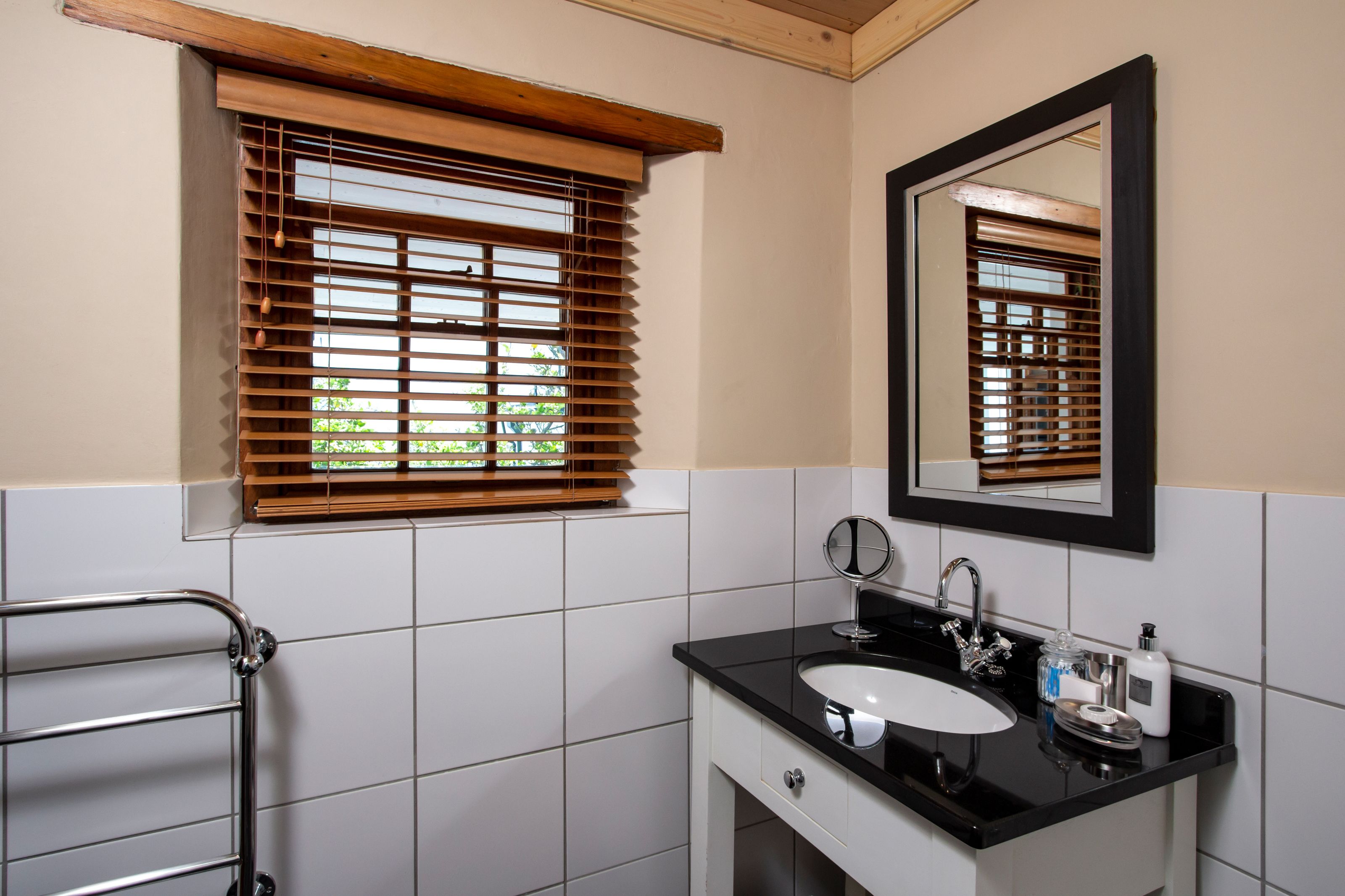 Un baño con un lavamanos negro, un espejo y persianas de madera.