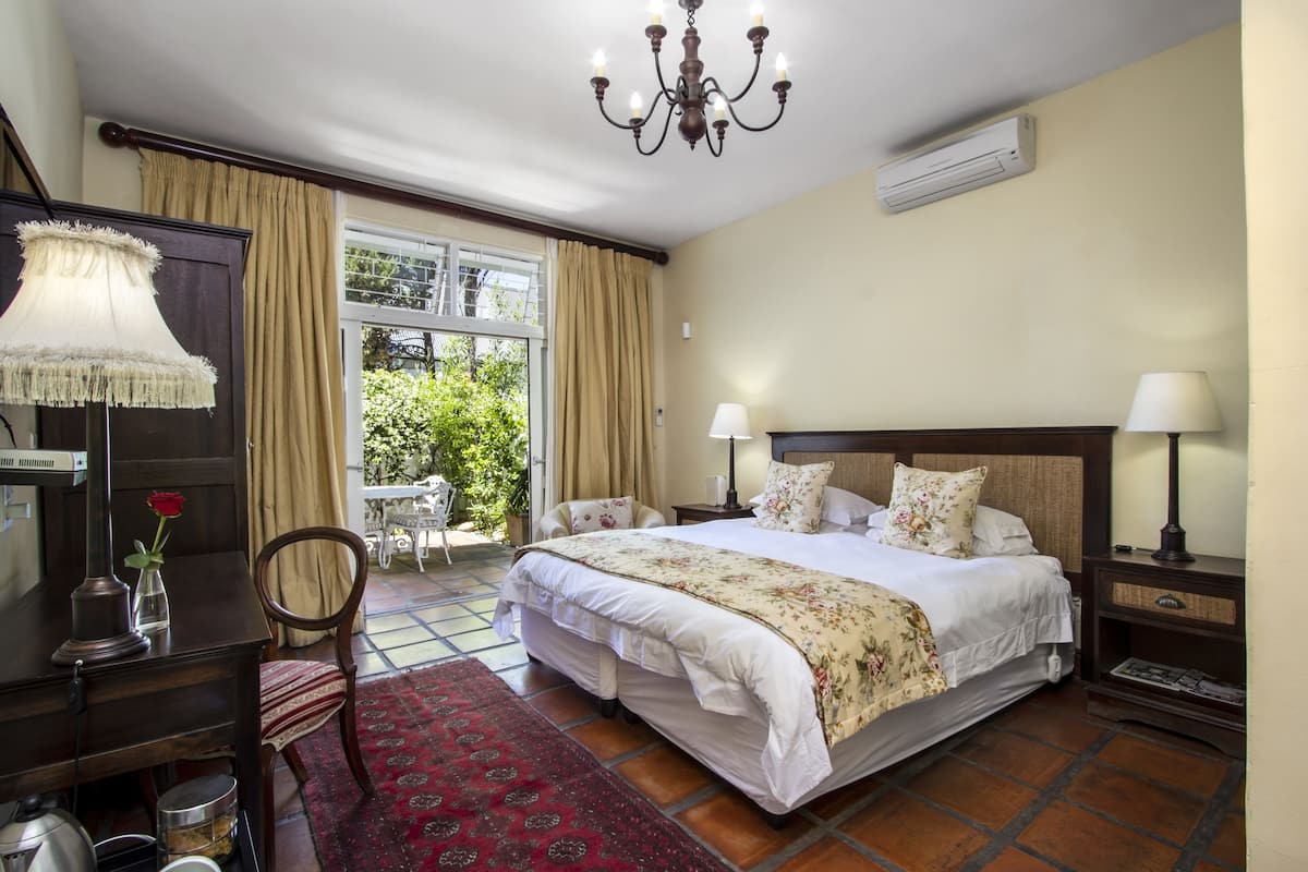 A well-appointed bedroom with a large bed, a chandelier, a desk with a lamp, and a view of greenery outside.