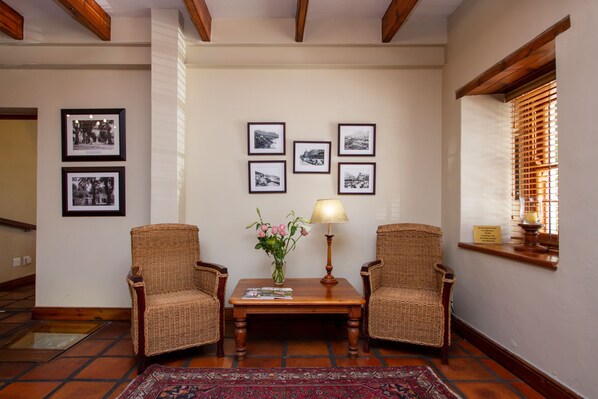 Una habitación con dos sillas de mimbre, una mesa de madera, un jarrón con flores y cuadros en la pared.