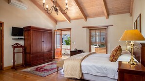 Un dormitorio con techo de madera, una cama con ropa blanca, un aparador de madera, un televisor y una ventana con persianas.