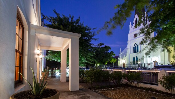 Un edificio blanco con un porche cubierto y una iglesia al fondo.