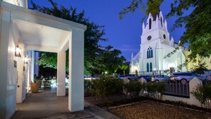 Una iglesia blanca con un campanario alto y un reloj, rodeada de árboles y coches estacionados.