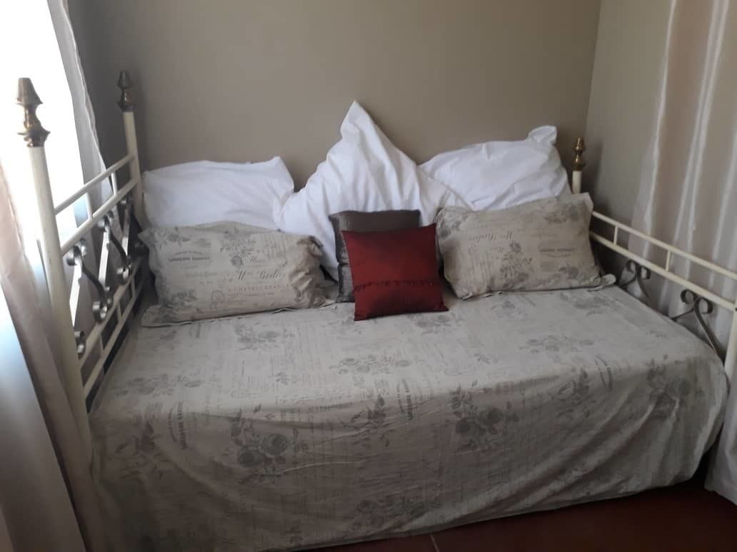 Una cama con una colcha estampada con flores, almohadas blancas y una almohada decorativa roja.