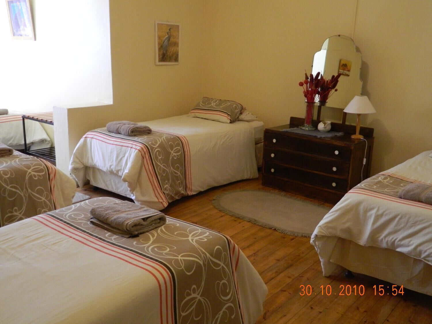 A hotel room with two beds, a dresser, a mirror, and a small table with a lamp.