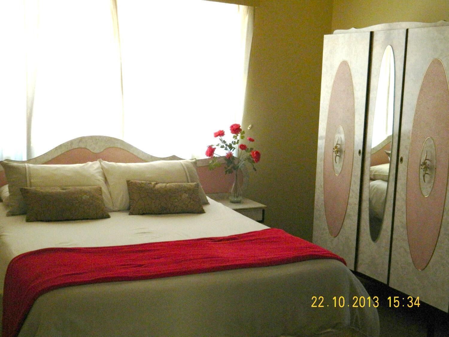 Una habitación de hotel con una cama, una mesita de noche, un jarrón con flores y un armario.