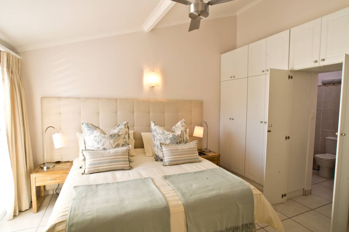 A bedroom with a large bed, bedside lamps, a nightstand, a ceiling fan, and a wardrobe.