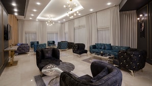 A modern living room with a high ceiling, recessed lighting, and a central chandelier. There are multiple seating areas with plush sofas and armchairs. - Nishan Hotel (Amman)