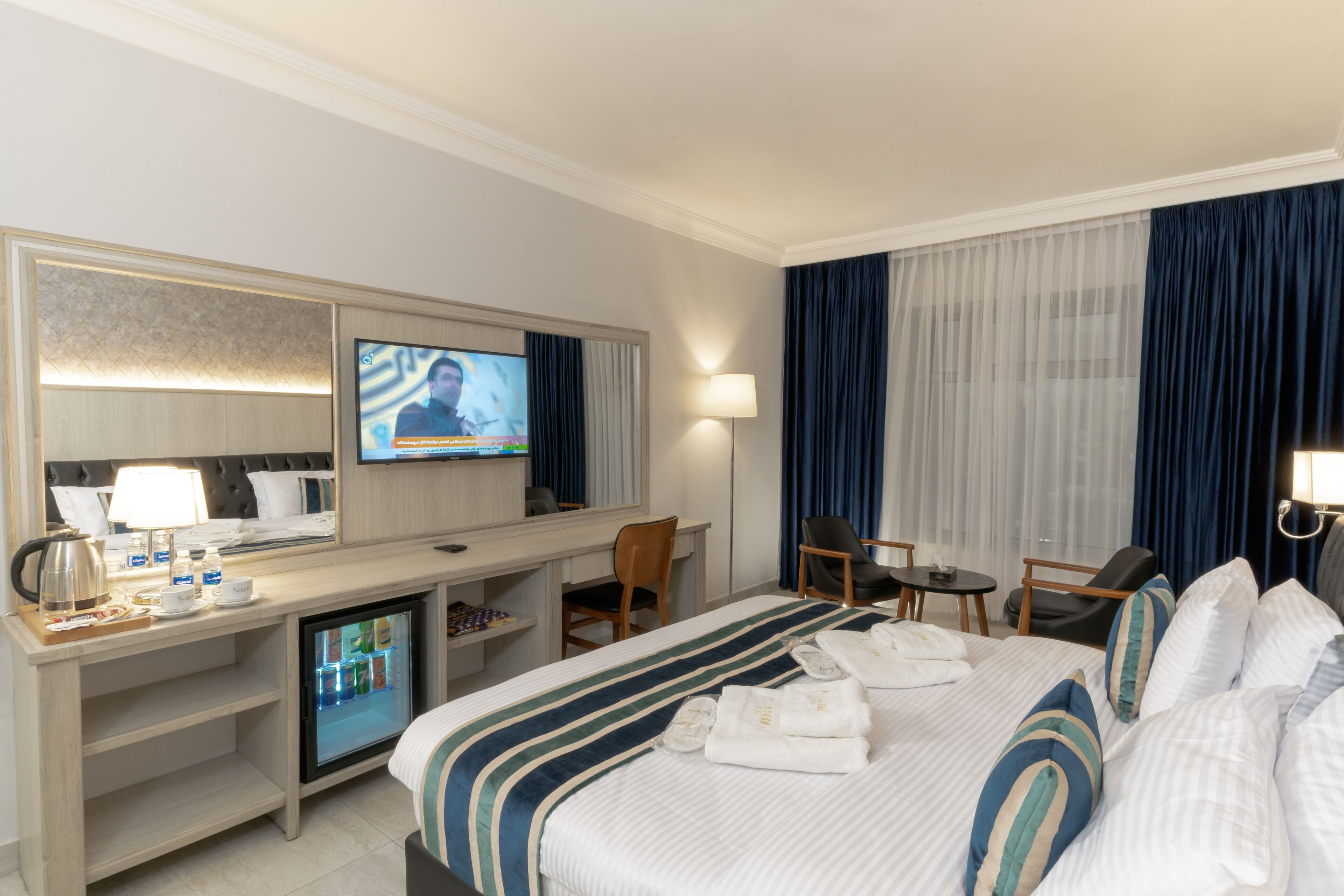A hotel room with a bed, a desk, a television, a mini-fridge, and a seating area with chairs.