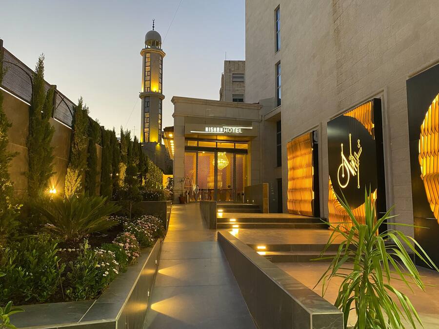 A hotel entrance with a modern design, a visible tower, and a well-lit pathway.