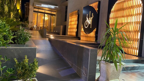 A modern hotel entrance with a reception desk, a large illuminated sign, and a well-lit pathway leading to the building. - Nishan Hotel (Amman)