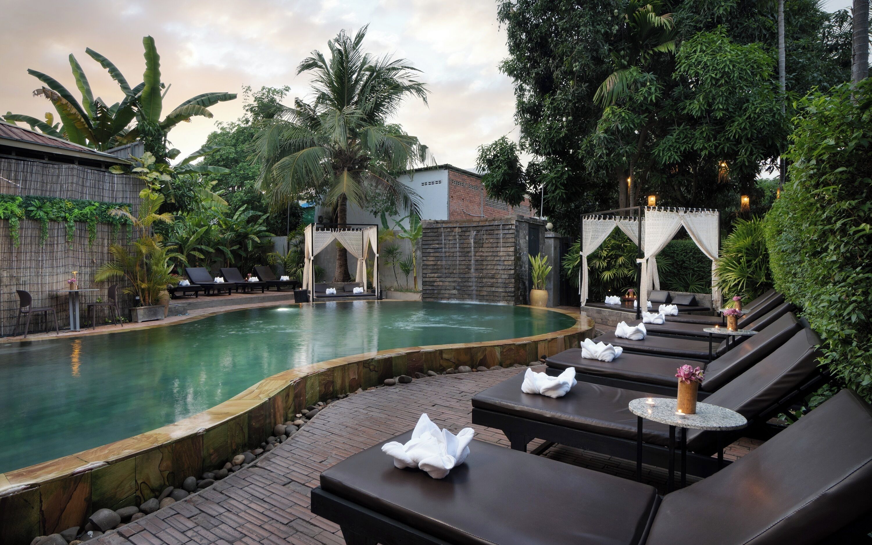 A pool area with lounge chairs, a small waterfall, and lush greenery.