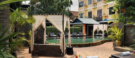 Zona junto a la piscina con sillas de descanso, un rincón cubierto para sentarse y una piscina.