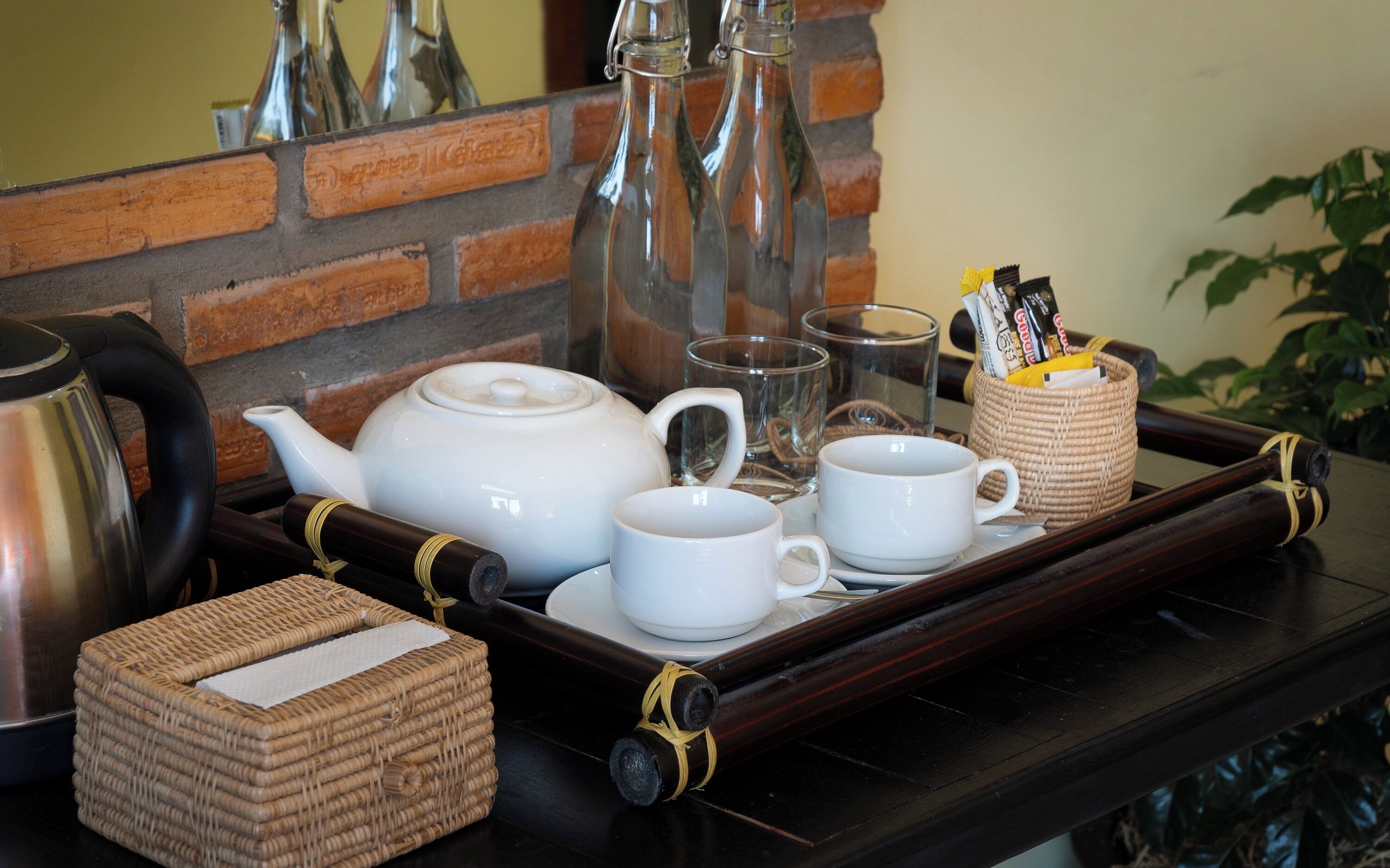 Un plateau avec une théière, des tasses, un verre et un panier, posé sur une table.