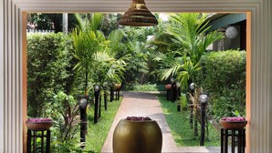 Un chemin bordé d’une végétation luxuriante et de jardinières décoratives, menant à l’entrée d’un bâtiment.