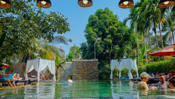 Un espace piscine avec une eau cristalline, entouré d’une végétation luxuriante et éclairé par des lampes suspendues qui créent une ambiance ombragée.