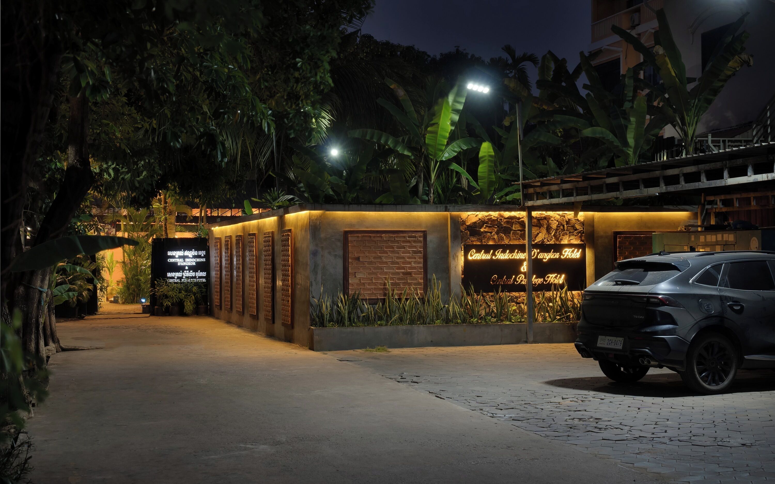 L’entrée d’un hôtel, avec une enseigne lumineuse, une allée pavée et une voiture garée.