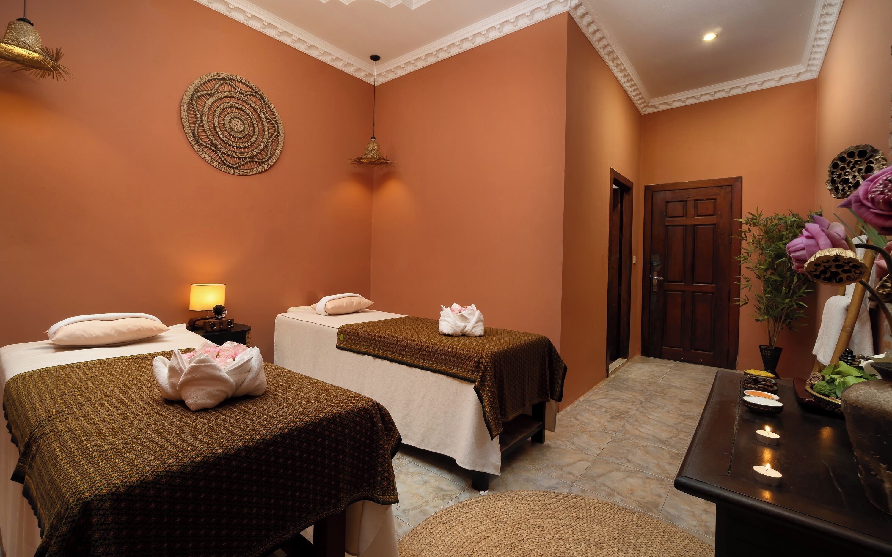 A spa room with two beds, a massage table, a wall-mounted decorative item, and a door leading to another room.