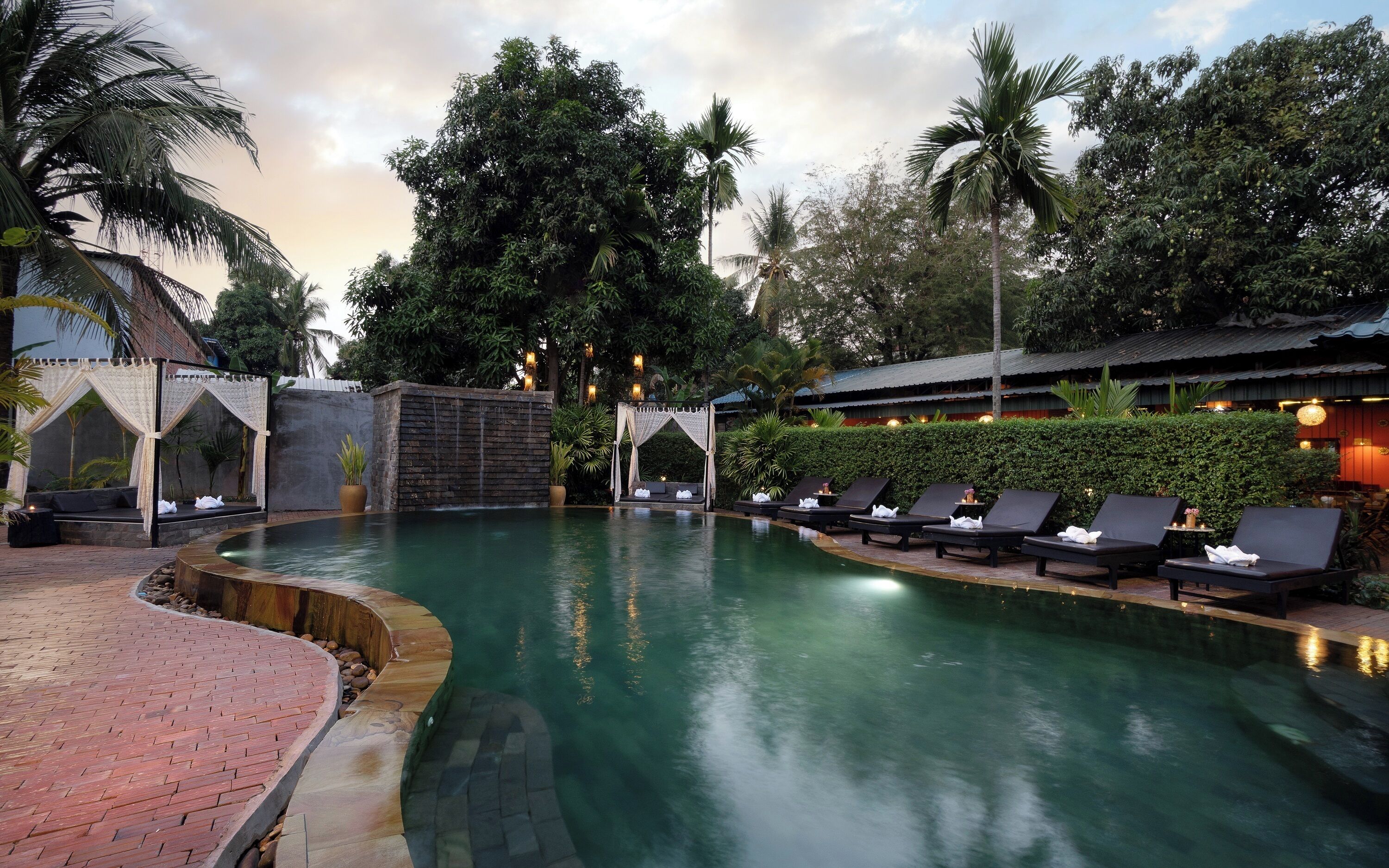 A pool area with lounge chairs, a brick pathway, and a waterfall feature.