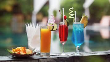 Four drinks with straws and garnishes on a table near a pool.