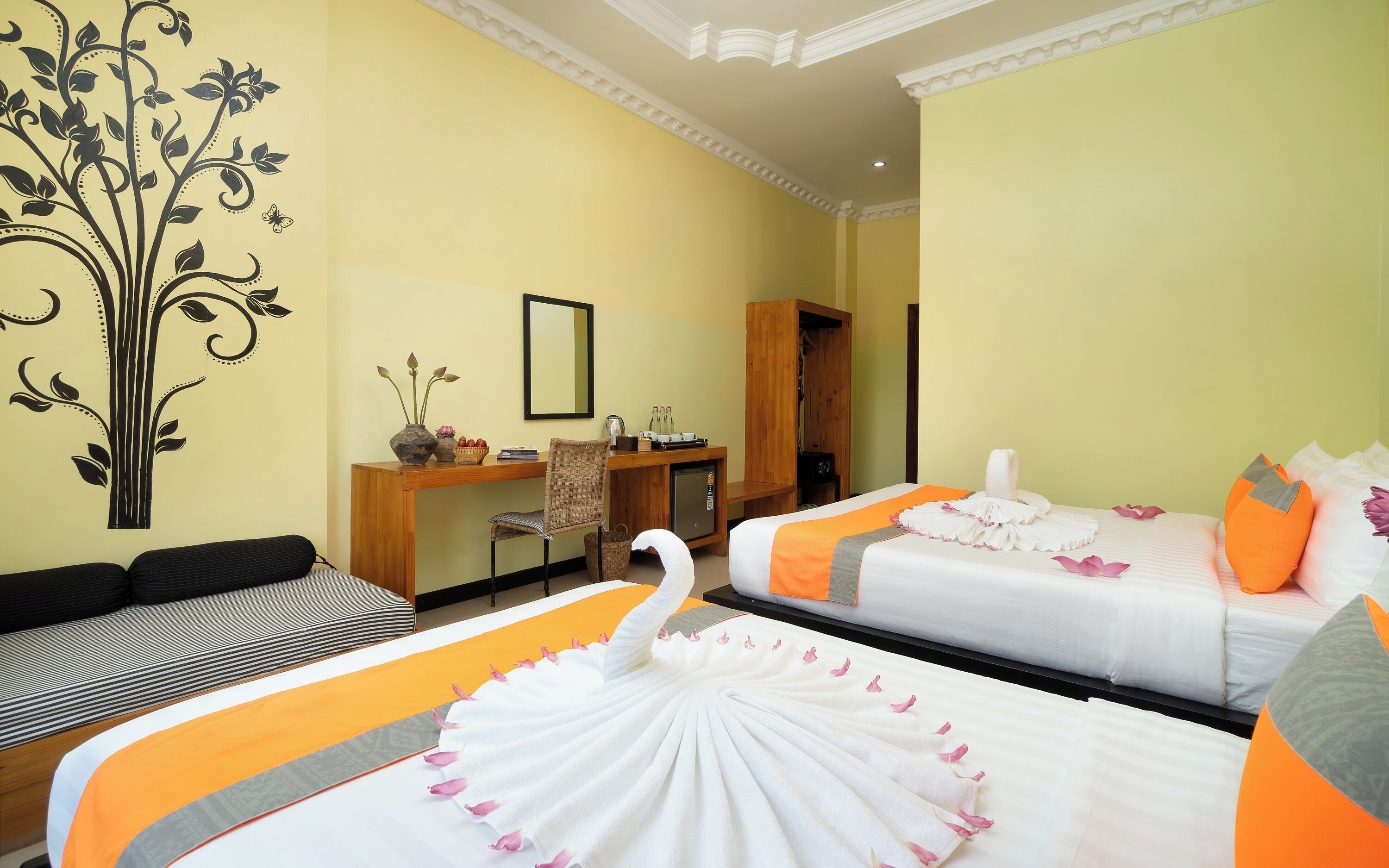 Ein Hotelzimmer mit zwei Betten, einem Schreibtisch mit Spiegel, einer kleinen Kühlbox und einem dekorativen Wandbild.