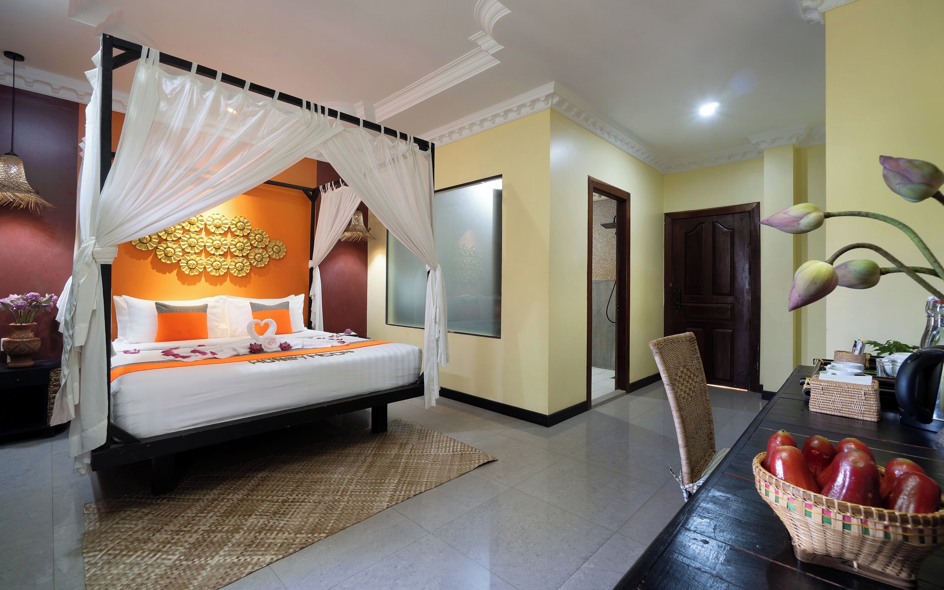 A hotel room with a bed, a dining table with fruits, and a decorative wall.