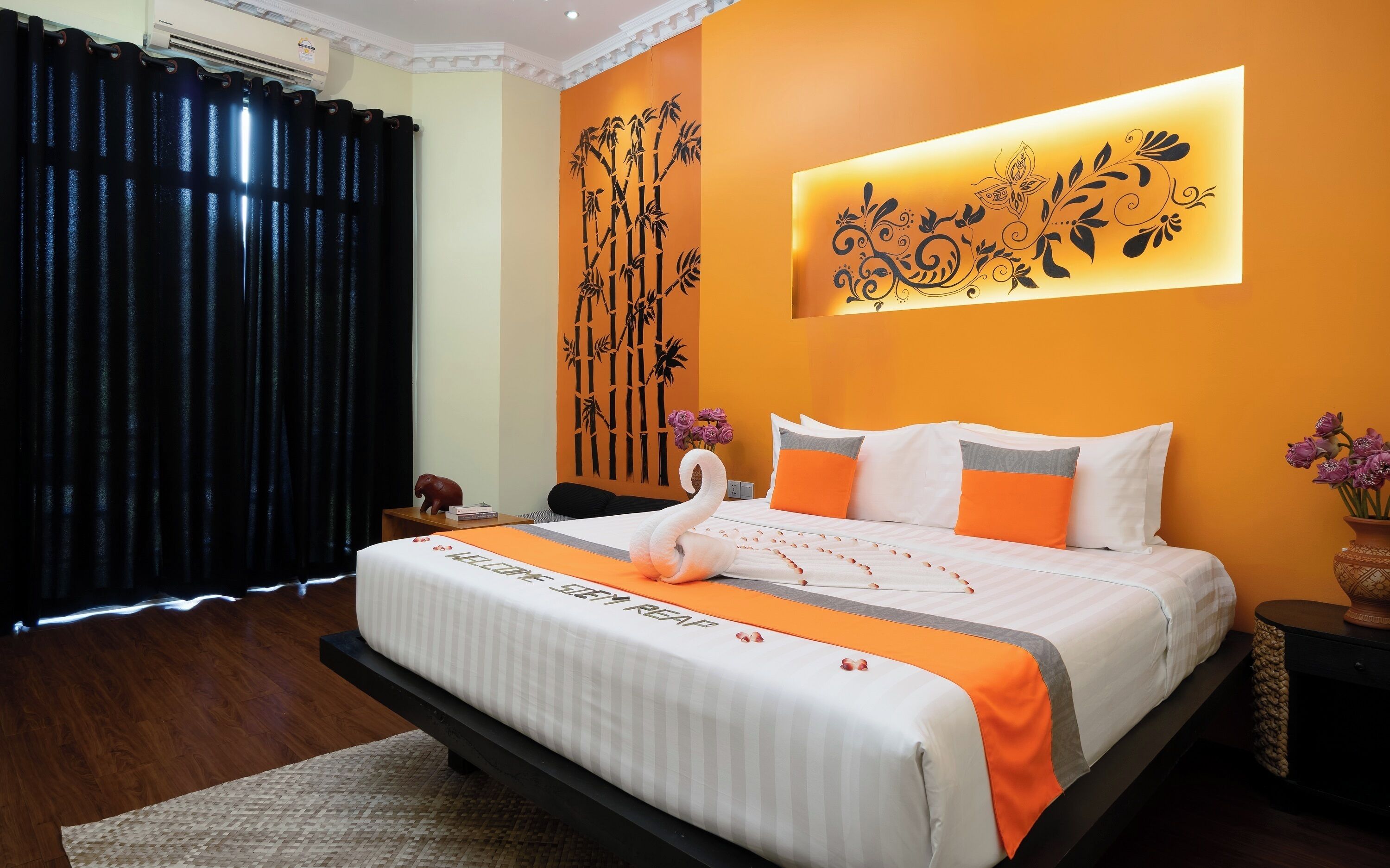 A hotel room with a bed, a wall-mounted air conditioner, and a decorative wall panel.