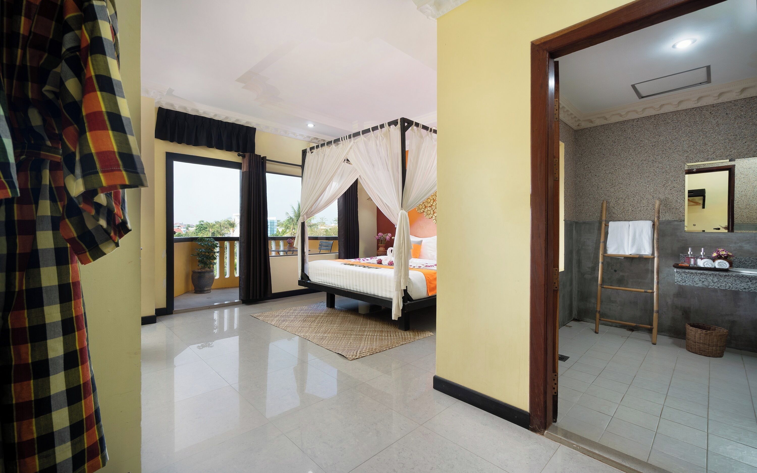 Ein Schlafzimmer mit Bett, Balkon, Badezimmer inklusive Spiegel und Blick ins Freie.