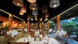 Un restaurant doté de nombreuses tables, de luminaires suspendus et offrant une vue sur la verdure environnante.