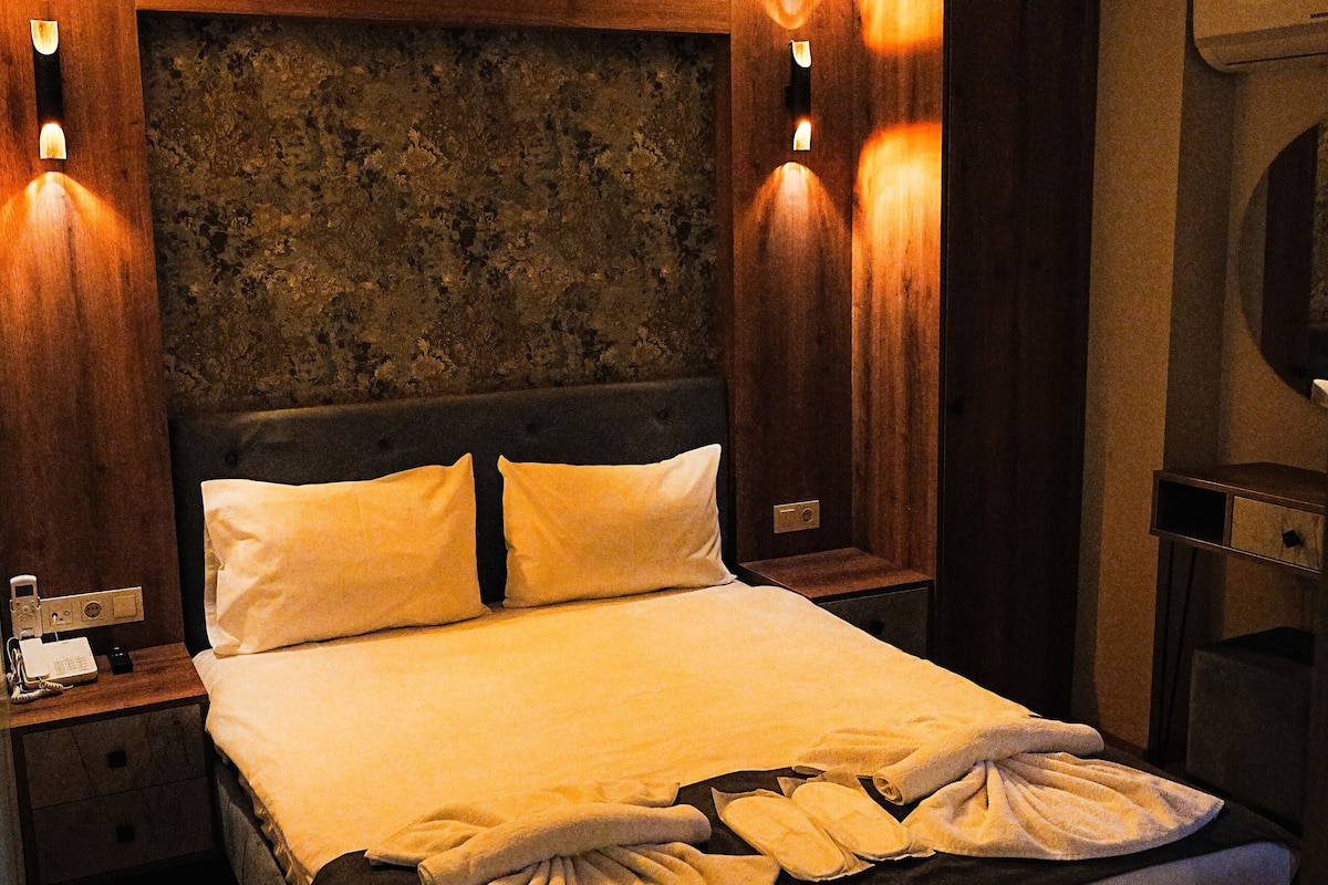 A hotel room with a large bed, wooden headboard, and wall-mounted sconces.