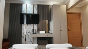 A modern hotel room with a bed, a desk with a flat-screen TV, a mirror, and a wooden door. - Reyyan Hotel (Istanbul)