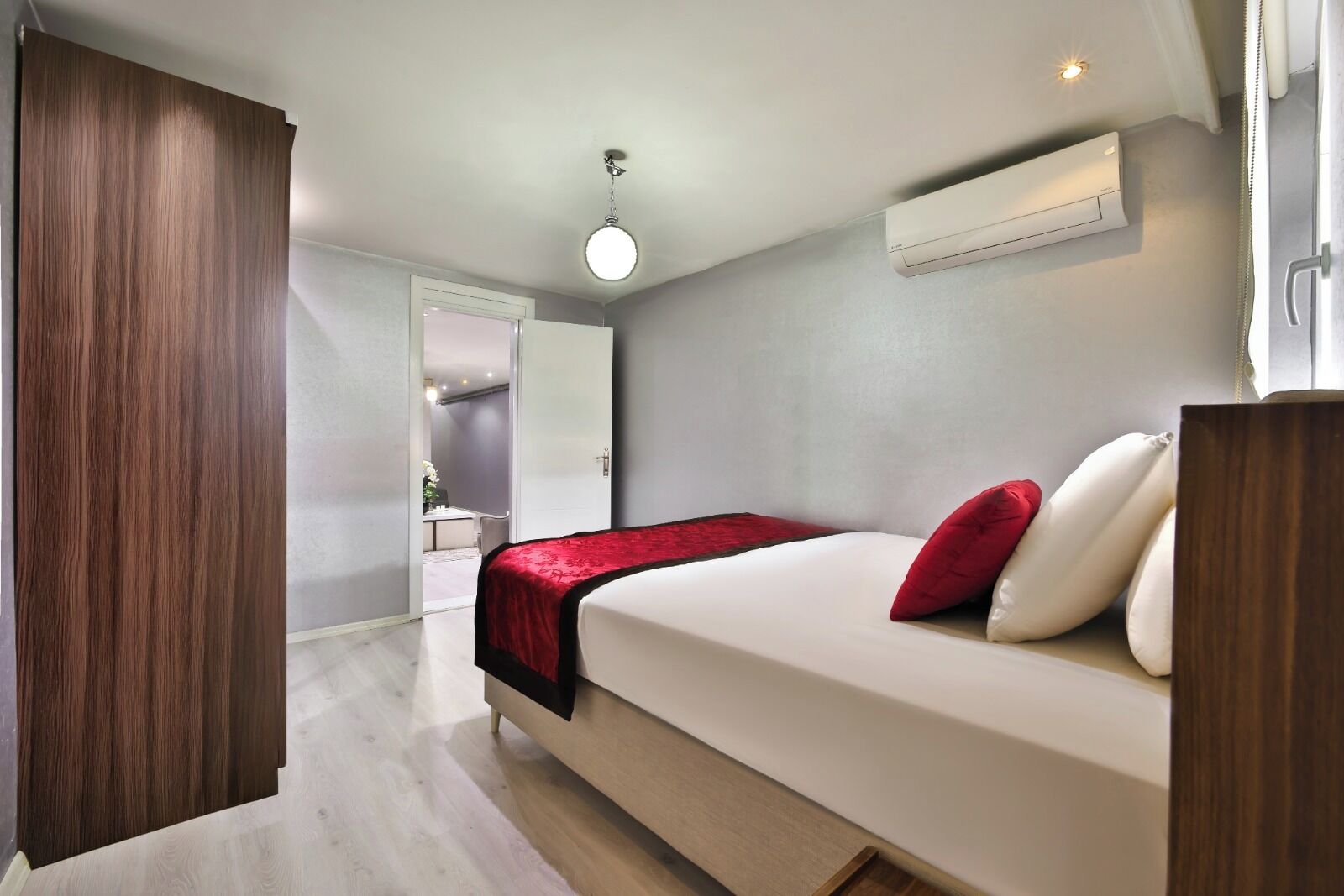 Een moderne hotelkamer met een bed, een rode plaid, een wit kussen, een houten garderobe en een plafondlamp.
