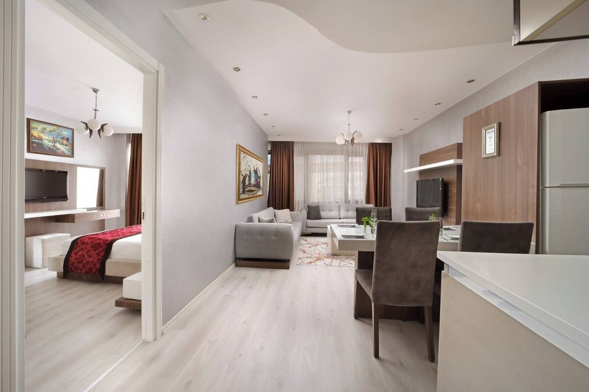 A modern hotel room with a sofa, dining table, and kitchen area.