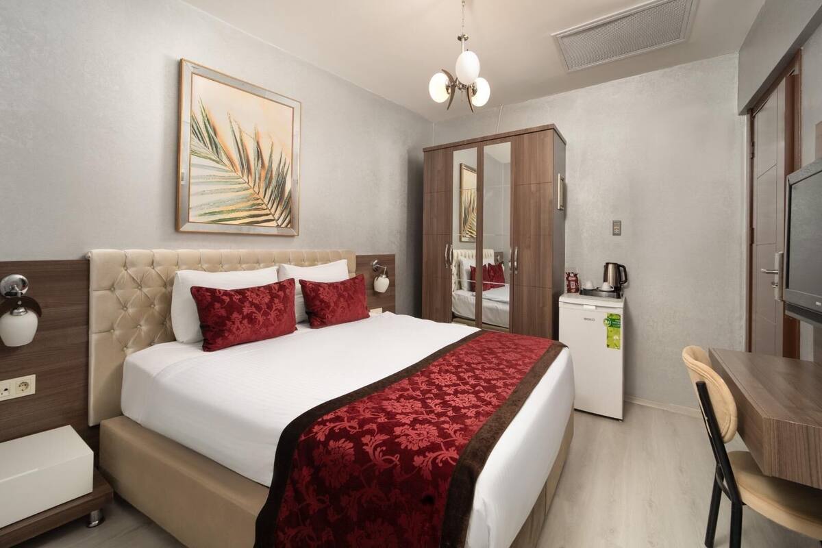 A hotel room with a bed, a desk, a minibar, and a large mirror.